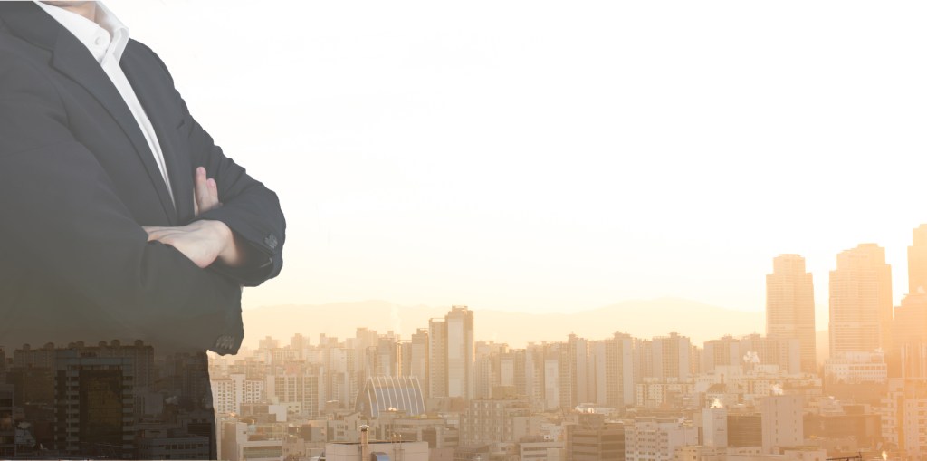 Double Exposure of Businessman Cityscape and Buildings in Background. Global Financial District with Commercial and Residential Real Estate. Investor in Suit with Arms Crossed. Success Concept.